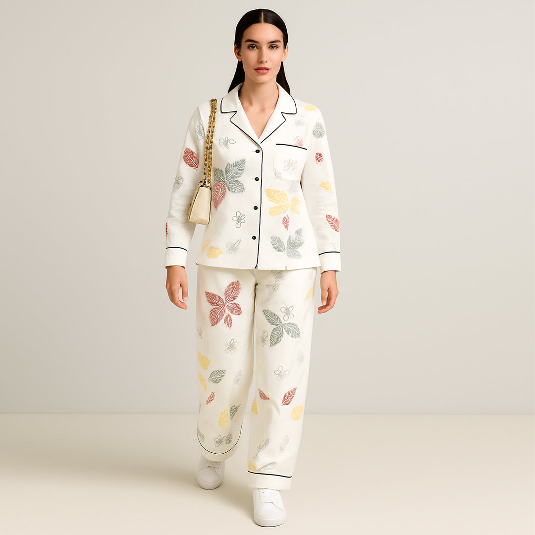 Woman wearing white pajama set with colorful leaf print and black piping, holding beige purse