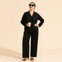 Woman wearing black solid two-piece suit with wide-leg pants, holding coffee, beige background