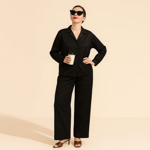 Woman wearing black solid two-piece suit with wide-leg pants, holding coffee, beige background