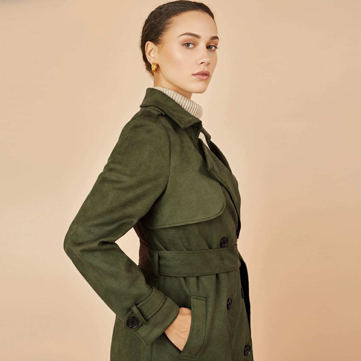 Woman wearing an olive green belted trench coat with button details and a beige turtleneck