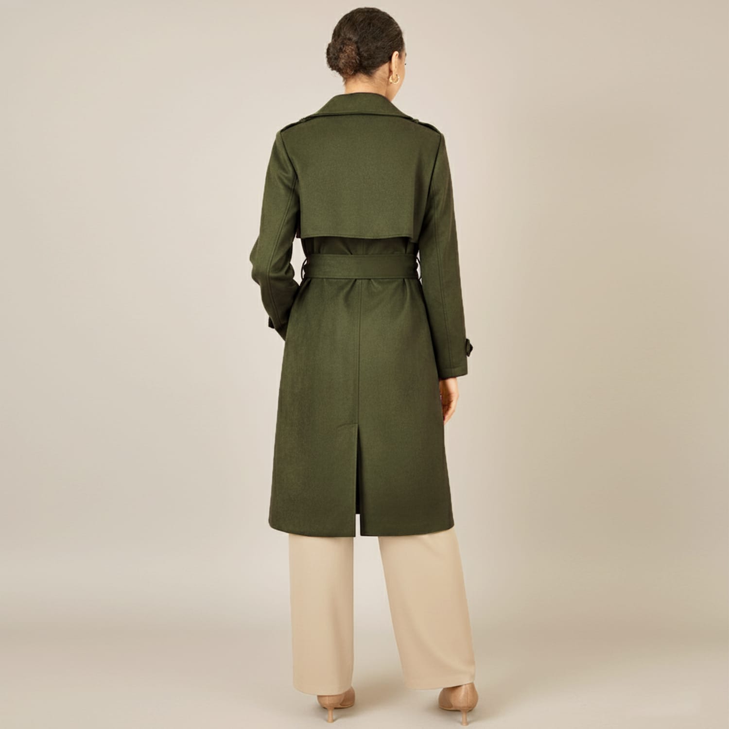 Woman wearing a long belted olive green coat and beige pants, shown from the back