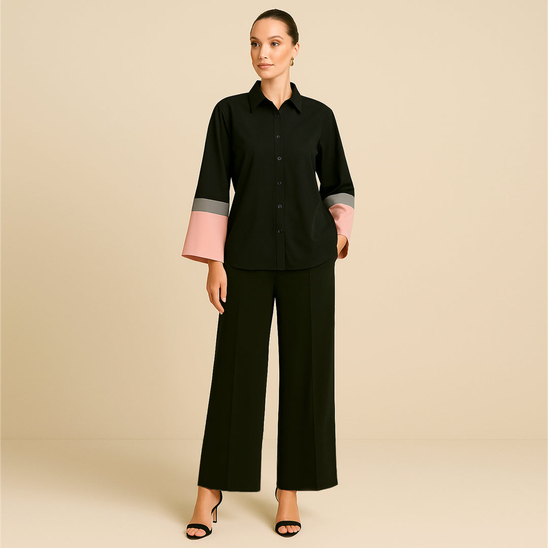 Woman modeling a black button-up shirt with pink and grey color block cuffs and wide-leg black pants