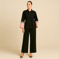 Woman modeling a black button-up shirt with pink and grey color block cuffs and wide-leg black pants