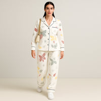 Woman wearing white pajama set with colorful leaf print and black piping, holding beige purse